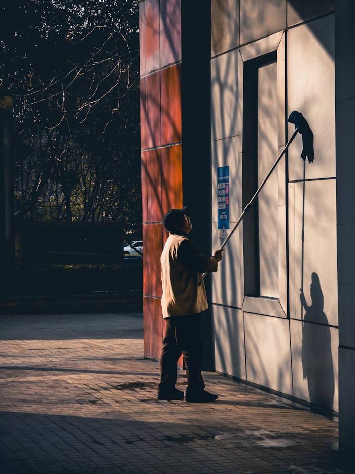 services-02 A man cleans the exterior of a building in a city, capturing a moment of urban maintenance.