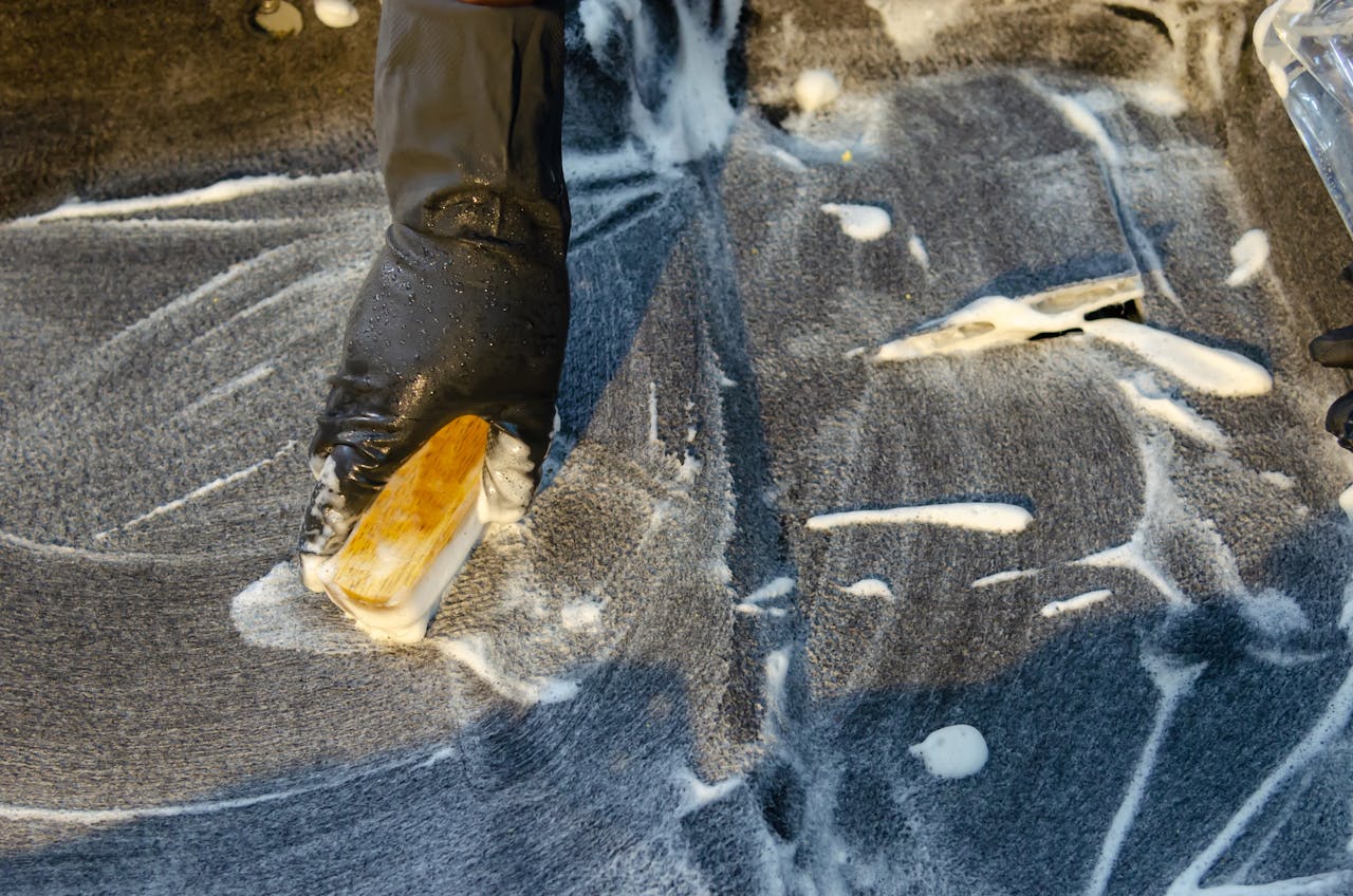 hero-img-02 A detailed view of cleaning in progress, focusing on a gloved hand using a brush with detergent on a surface.